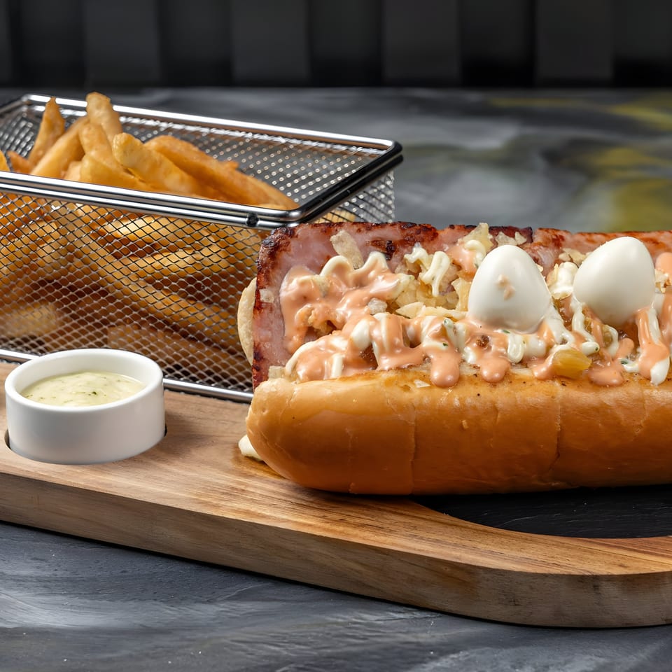 Colombian hot dog with quail eggs, sauces, and crushed chips, served with fries and a dipping sauce.