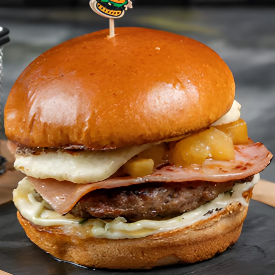A Colombian burger with ham, melted cheese, pineapple chunks, and a burger patty on a brioche bun.