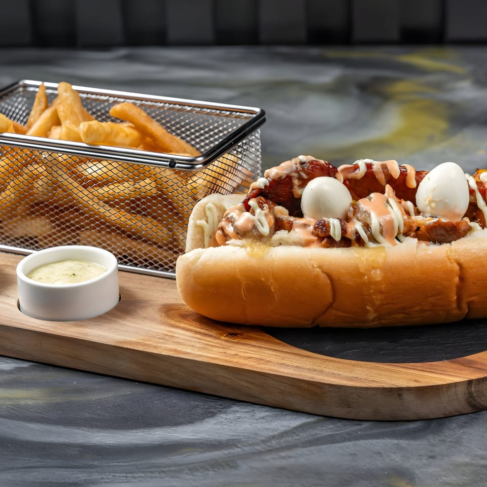Colombian hot dog with quail eggs and sauces, served with a side of fries and dipping sauce.